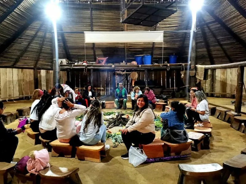Mujeres reunidas en círculo dentro de una maloca durante una actividad comunitaria